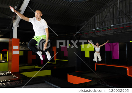 Joyful young man jumping on trampolines in colorful amusement park 129032905