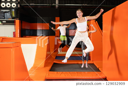 Happy girl bouncing on trampoline in indoor amusement park Happy girl bouncing on trampoline in indoor amusement park 129032909