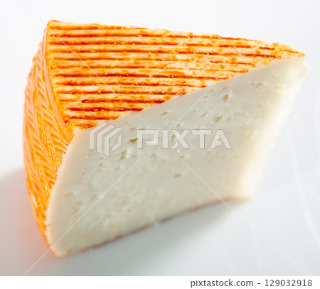 Appetizing slice of semi-soft cheese on a white surface 129032918