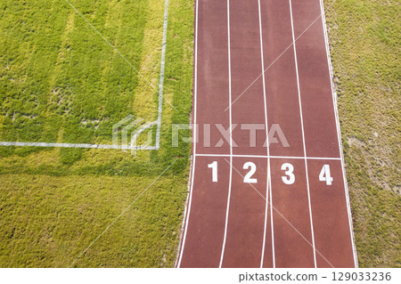 Top view of red running tracks and green grass lawn. Infrastructure for sports activities. 129033236