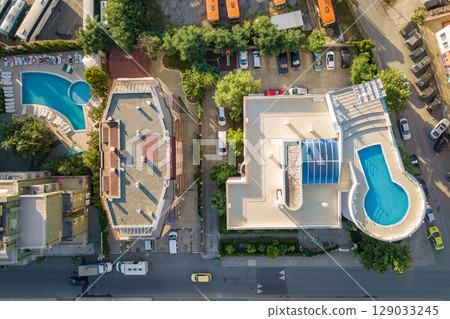 Top down aerial view of hotels roofs, streets with parked cars and swimming pools with blue water in resort city near the sea Top down aerial view of hotels roofs, streets with parked cars and swimming pools with blue water in resort city near the sea 129033245
