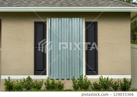 Storm resistant steel shutters cover windows of Florida house as precaution before hurricane. Home prepared for extreme weather Storm resistant steel shutters cover windows of Florida house as precaution before hurricane. Home prepared for extreme weather 129033366