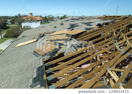 Ruined rooftop in need of repair. Wind damaged house roof with missing asphalt shingles after hurricane Ian in Florida Ruined rooftop in need of repair. Wind damaged house roof with missing asphalt shingles after hurricane Ian in Florida 129033415