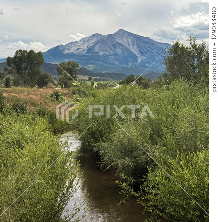 Peaceful Stream Winding Through Lush Valley Below Majestic Mountain 129033480