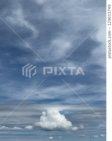Towering Cumulus Cloud Beneath Swirling Blue and Gray Sky 129033749