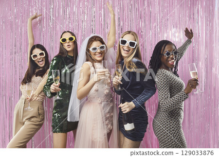 Cheerful diverse stylish women in glamorous dresses celebrating bachelorette party with champagne. Cheerful diverse stylish women in glamorous dresses celebrating bachelorette party with champagne. 129033876