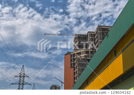 Tall buildings are being constructed with cranes against a bright blue sky 129034182