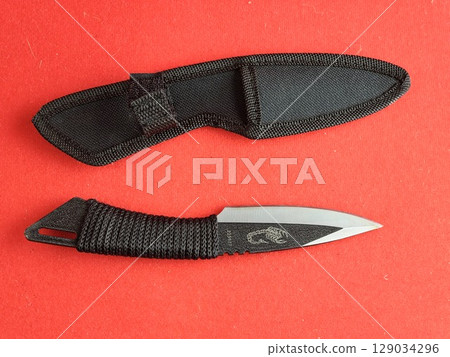 Throwing knife scorpion and black case. Traditional Japanese cold weapon on red background. Throwing knife scorpion and black case. Traditional Japanese cold weapon on red background. 129034296