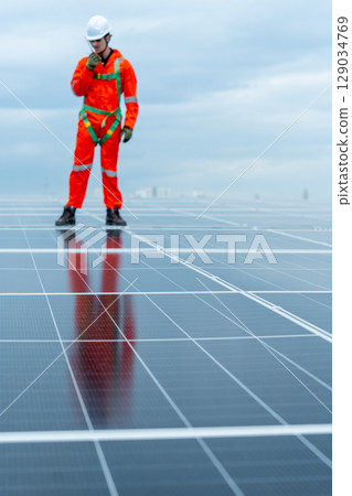 Vertical image with main focus on solar cell panel with technician worker or professional engineer stand and use walkie-talkie during check and maintenance. 129034769