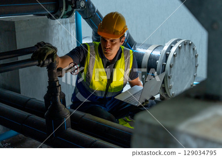 Factory worker man use laptop to check pipe system under part of factory building. 129034795