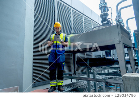 Factory worker or engineer man use tablet to working and stand near temperature system controling in area of factory. Factory worker or engineer man use tablet to working and stand near temperature system controling in area of factory. 129034796