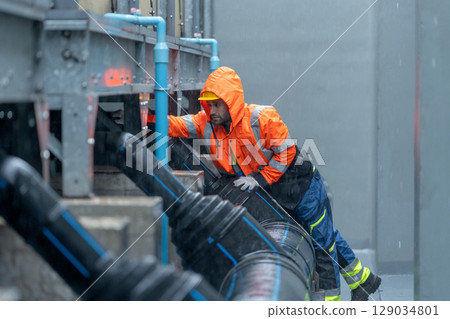 Factory worker or technician with raincoat check and maintenance pipe system in area of factory building during raining. Factory worker or technician with raincoat check and maintenance pipe system in area of factory building during raining. 129034801