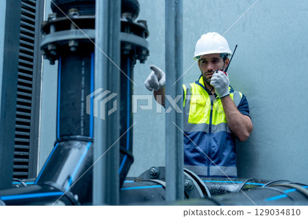 Engineer or technician worker use walkie talkie to contact co-worker also point to pipe during work with steel pipe system of factory building. Engineer or technician worker use walkie talkie to contact co-worker also point to pipe during work with steel pipe system of factory building. 129034810