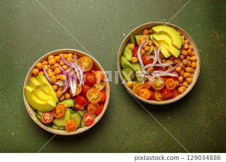 Two bowls with vibrant vegetarian chickpea salad with fresh vegetables in ceramic bowls top view on green background 129034886
