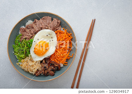 Traditional korean bibimbap with fried egg, beef and vegetables and other toppings top view on light background, space for text Traditional korean bibimbap with fried egg, beef and vegetables and other toppings top view on light background, space for text 129034917