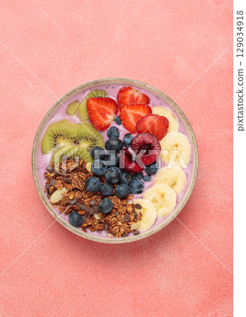 Delicious acai bowl with fresh fruits and granola in white ceramic bowl on pink table top view, healthy breakfast or snack Delicious acai bowl with fresh fruits and granola in white ceramic bowl on pink table top view, healthy breakfast or snack 129034918