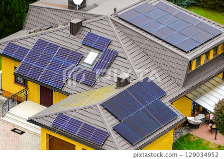 Modern Yellow Brick House with Multiple Roof-Mounted Solar Panels for Sustainable Energy Use 129034952