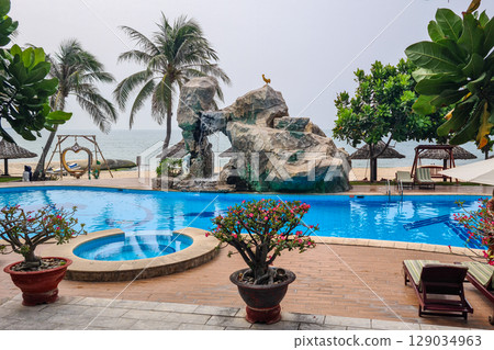 Tropical Seaside Resort Pool with Palm Trees, Rock Waterfall, and Relaxing Oceanfront Ambiance 129034963