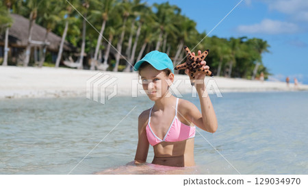 Girl holds starfish in clear water at tropical beach enjoying summer vacation 129034970