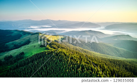Breathtaking aerial view of mountain landscape at sunset. Golden light bathes rolling hills and lush forests, creating serene and idyllic scene. Distant mountains adding depth to picturesque vista. 129035008