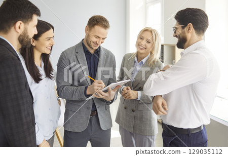 Group of cheerful business people discussing work project standing in office during a meeting. Group of cheerful business people discussing work project standing in office during a meeting. 129035112