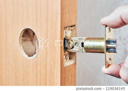 Latch bolt mechanism being inserted into door edge mortise for lock installation showing positioning process and latch faceplate alignment. 129036145