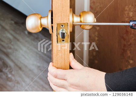 Doorknob mechanism being secured with screwdriver into latch plate of wooden door during installation of standard interior lockset. 129036148