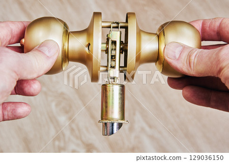 Door lockset components held by hands during assembly showing latch mechanism and alignment of parts before door knob installation. 129036150
