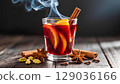 Close-up of a glass of hot mulled wine with delicious steam rising from it. The drink is a rich red color, garnished with orange slices and cinnamon sticks. Spices such as star anise, cinnamon sticks, 129036166