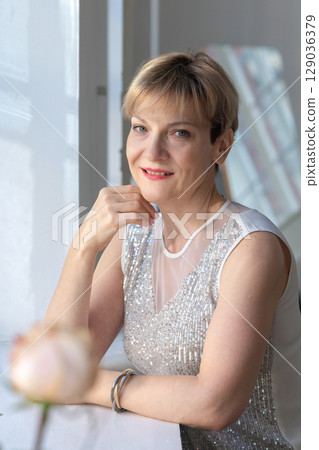 Portrait of smiling woman in festive clothes against a gray wall in a bright sunny room. Vertical photo. High quality photo 129036379