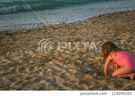 Little girl in swimsuit playing alone on an empty sandy beach 129040283
