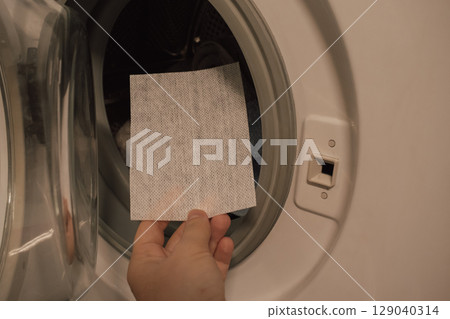 Female hand placing color-catching sheet into washing machine 129040314