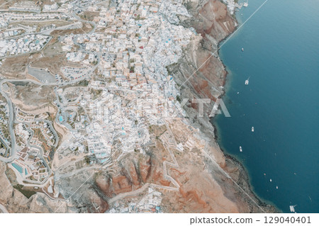 Drone photo of Oia, Santorini showing white houses built on steep cliffs by the sea Drone photo of Oia, Santorini showing white houses built on steep cliffs by the sea 129040401