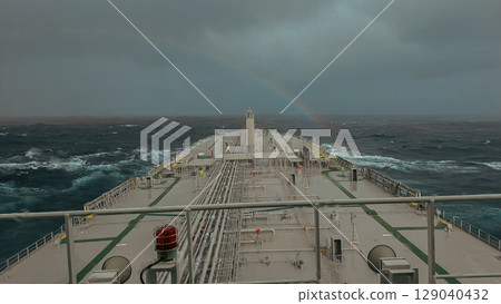 Commercial fleet under cloudy sky, large tanker beneath rainbow 129040432