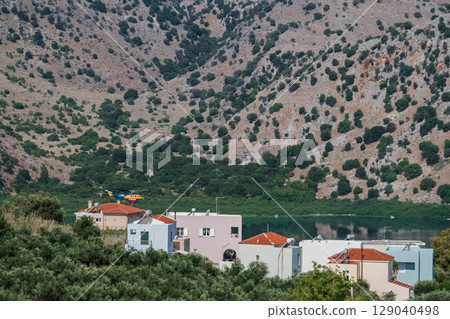 Firefighting helicopter flying low over residential houses near a lake to collect water 129040498