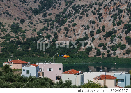 Firefighting helicopter flying low over residential houses near a lake to collect water Firefighting helicopter flying low over residential houses near a lake to collect water 129040537