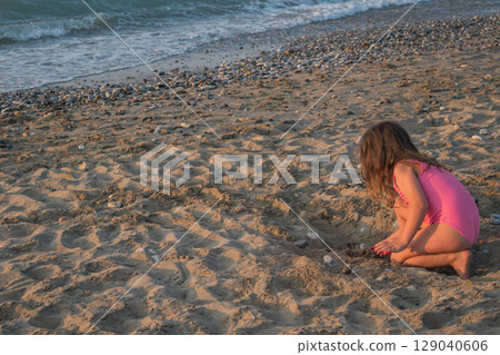 Little girl playing alone on the beach, digging a hole in the sand Little girl playing alone on the beach, digging a hole in the sand 129040606