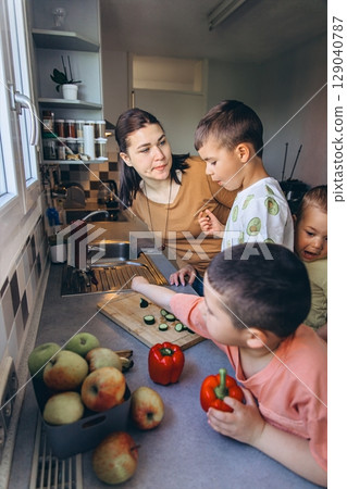 Happy mother spending time with her three young sons in the kitchen. Kids explore fruits and vegetables by the window. Family warmth, parenting, and healthy home life Happy mother spending time with her three young sons in the kitchen. Kids explore fruits and vegetables by the window. Family warmth, parenting, and healthy home life 129040787
