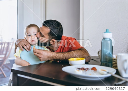 Father lovingly kisses his toddler on the cheek during breakfast time at home. A warm and emotional moment between parent and child in a cozy kitchen setting 129040817