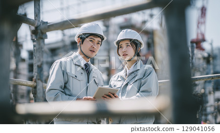 Male and female business people looking at a tablet at a construction site 129041056