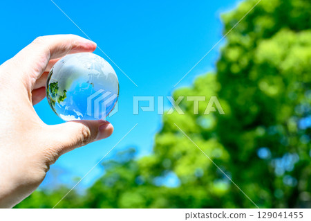 Holding the Earth up against the beautiful blue sky and fresh greenery, Earth's normal color 129041455