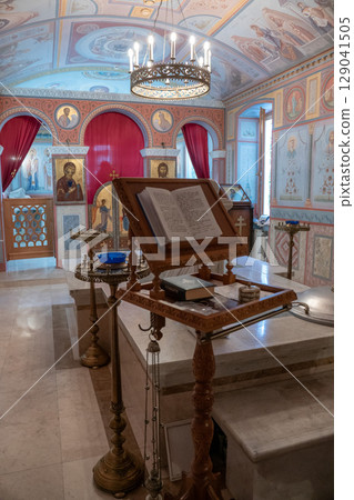 Interior of an Orthodox church richly decorated with religious icons, red curtains, wall frescoes, and a central chandelier 129041505