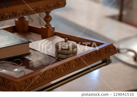 Close-up of an Orthodox prayer book, placed on a carved wooden lectern inside a church, accompanied by a small ornate container and baptismal crosses Close-up of an Orthodox prayer book, placed on a carved wooden lectern inside a church, accompanied by a small ornate container and baptismal crosses 129041510