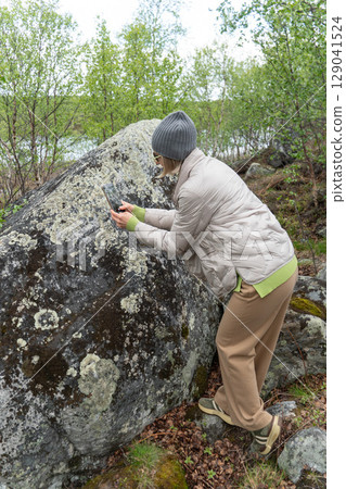 A woman photographs a moss-covered boulder in a lush northern forest using her smartphone A woman photographs a moss-covered boulder in a lush northern forest using her smartphone 129041524