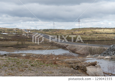 A remote road stretches through the arctic tundra landscape with sparse traffic and utility poles lining the way A remote road stretches through the arctic tundra landscape with sparse traffic and utility poles lining the way 129041555
