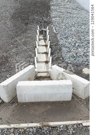 Concrete drainage channel with embedded plastic pipe for stormwater management, set against gravel and gabion-covered slope Concrete drainage channel with embedded plastic pipe for stormwater management, set against gravel and gabion-covered slope 129041564