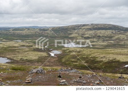 Scenic Arctic tundra landscape near Teriberka, Russia, with moss-covered hills, small lakes, and piles of stones under dramatic cloudy skies 129041615