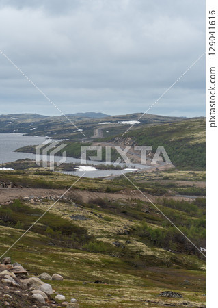Scenic Arctic tundra landscape near Teriberka, Russia, with moss-covered hills, small lakes, and piles of stones under dramatic cloudy skies 129041616
