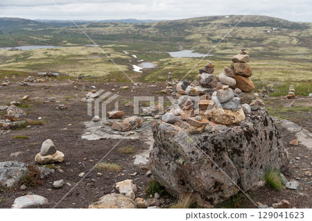 Multiple stone cairns are carefully balanced on a rocky tundra plateau overlooking mossy hills, lakes, and snowy patches near Teriberka, Russia Multiple stone cairns are carefully balanced on a rocky tundra plateau overlooking mossy hills, lakes, and snowy patches near Teriberka, Russia 129041623