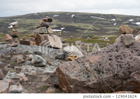 Stacked stone cairns standing on rocky tundra in Teriberka, Russia, with snow-dotted hills in the background Stacked stone cairns standing on rocky tundra in Teriberka, Russia, with snow-dotted hills in the background 129041624